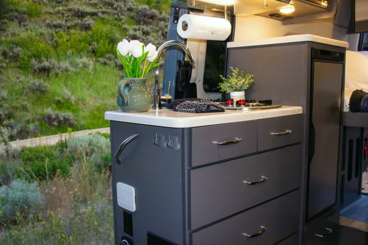 This rv rental features a modern, functional kitchen with a sink, stove, and ample storage, providing comfort amidst scenic outdoor views.. Mercedes-Benz Sprinter 4x4 2022
