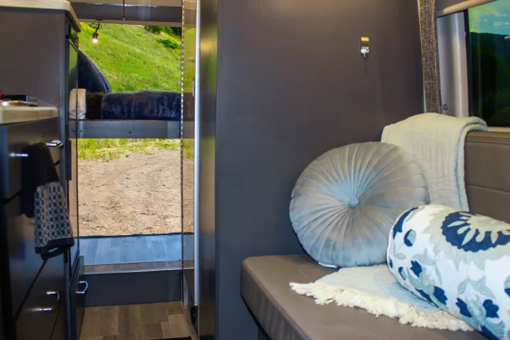 Inside an RV rental: a plush lounge, elevated bunk, and the rear open to a dirt road & green hills.. Mercedes-Benz Sprinter 4x4 2022