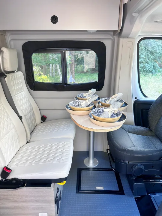 Spacious RV rental interior features white padded bench seating, a round dining table, and a dark gray driver's seat.. Winnebago Solis 2022