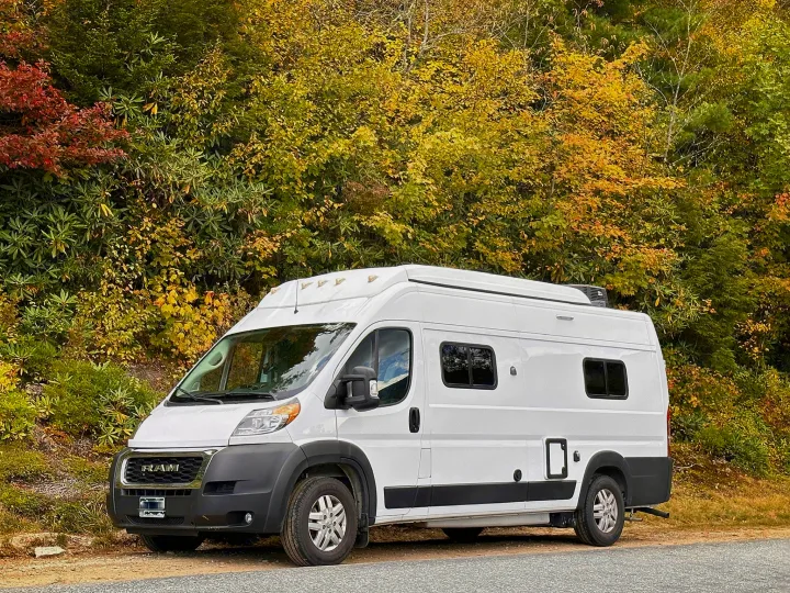 Bright white RV rental camper van parked beside a road, framed by vibrant autumn foliage.. Winnebago Solis 2022