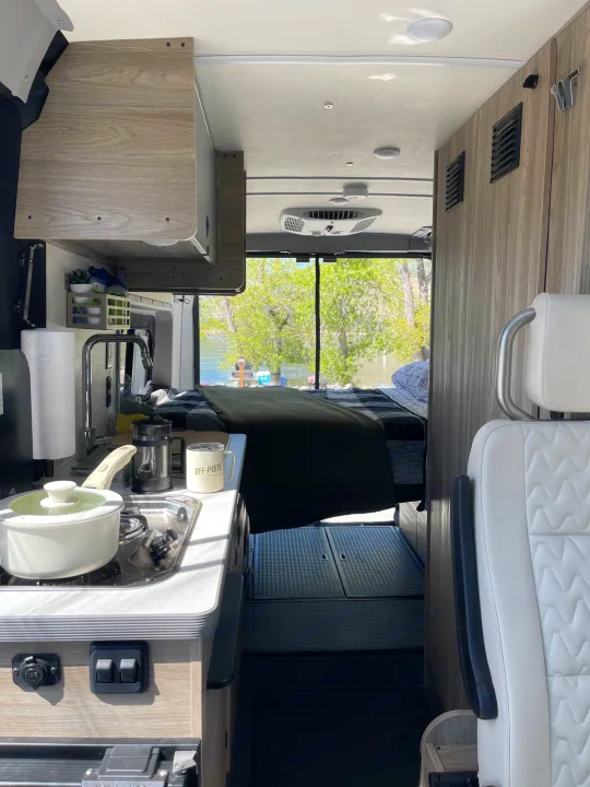 Cozy RV rental: compact kitchen with stove, sink, and coffee, plus a comfortable bed overlooking a serene river.. Winnebago Solis 2023