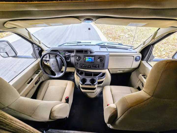 Step inside this RV rental! The photo captures the well-equipped driver's cockpit, passenger seat, dashboard, and open road ahead.. ALP Adventurer 19RD 2021