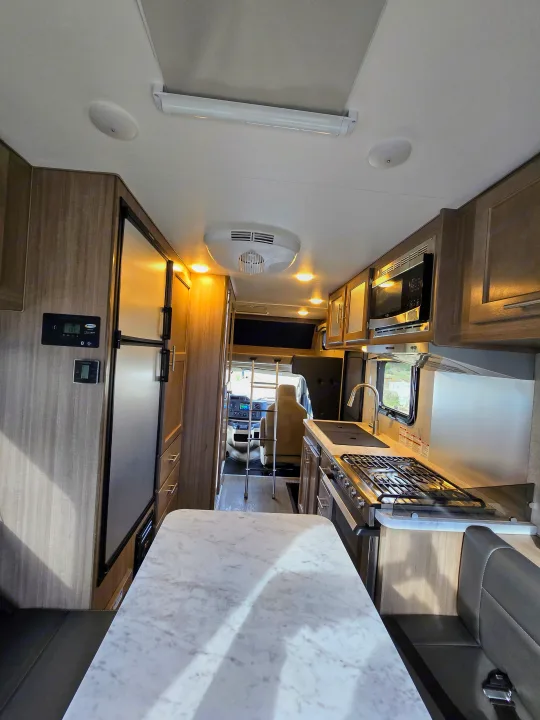 View inside an RV rental: kitchen with stove & microwave, fridge, dining table, and front cab.. ALP Adventurer 19RD 2021