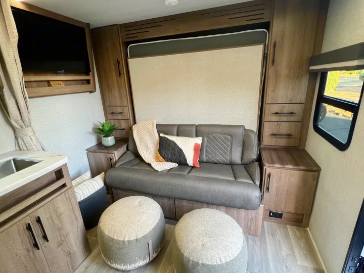 Cozy RV rental interior with a gray sofa, convertible Murphy bed, TV, and built-in cabinetry for comfortable travel.. Grand Design Imagine XLS 2024