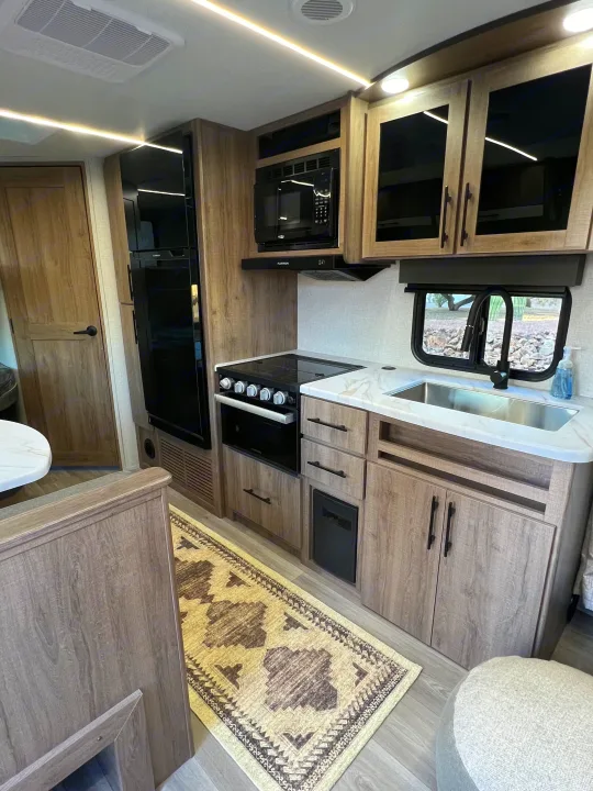 Modern RV rental kitchen with full appliances, ample storage, and bright lighting, perfect for travel adventures.. Grand Design Imagine XLS 2024