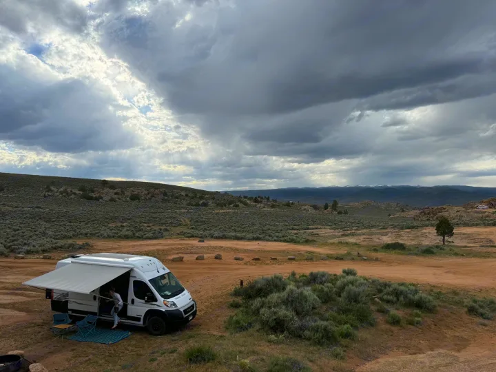 An RV rental offers adventure! White camper van parked in a scenic desert landscape with dramatic, sunlit clouds.. Winnebago Solis 2023