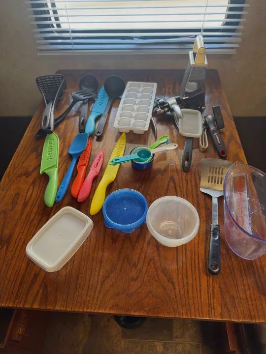 RV rental kitchen essentials: spatulas, knives, measuring cups, and containers neatly arranged on a wooden table for compact travel.. Forest River Salem Cruise Lite 2017