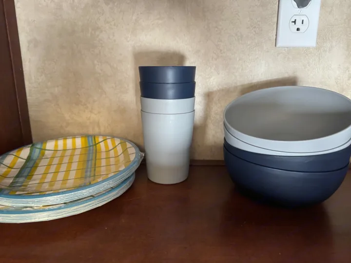 RV rental kitchen setup: blue & white reusable cups/bowls, plus plaid paper plates, on a wooden counter near an outlet.. Forest River Salem Cruise Lite 2017