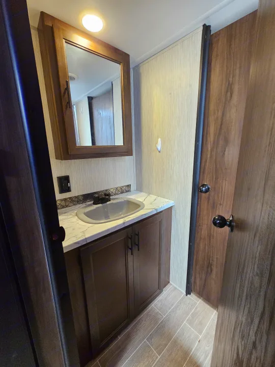 An RV rental washroom with a vanity, sink, mirror, and wood-look tiled flooring. Functional and compact.. Forest River Cherokee Grey Wolf 2021