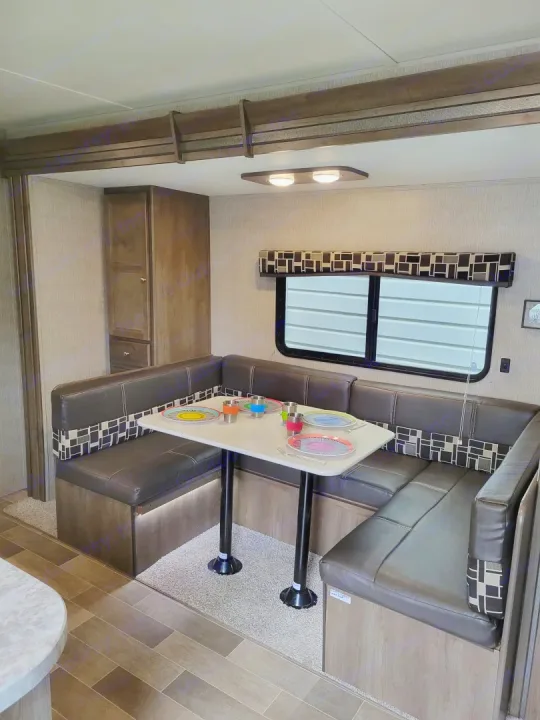This RV rental interior features a spacious U-shaped dinette with comfortable seating and a set table, perfect for dining.. Keystone Coleman Lantern 2019