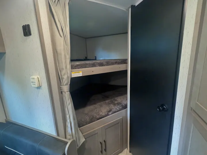 Inside this RV rental, comfortable bunk beds with privacy curtains, a thermostat, and a black door are visible.. Dutchmen Kodiak Ultra Lite 2022