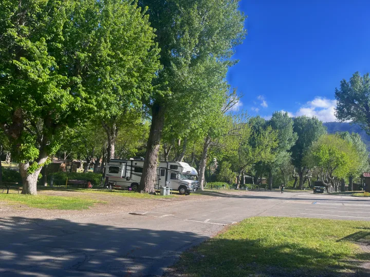 Sun-drenched RV park with two RVs nestled among green trees. An idyllic setting for your next **RV rental** escape.. Forest River Sunseeker LE 2023