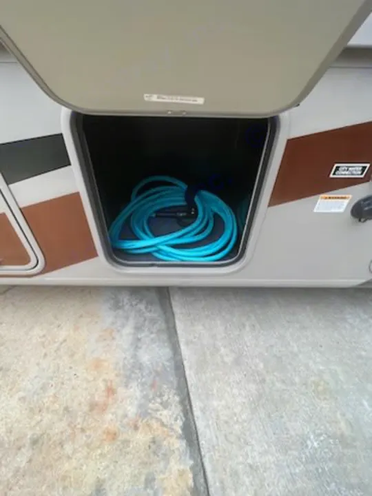 An RV rental's side storage compartment holds a coiled blue water hose, ready for use at a campsite.. Forest River Coachmen Pursuit 2017