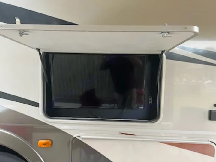 This RV rental features an outdoor TV in an open side compartment for entertainment, with a reflection on screen.. Forest River Coachmen Pursuit 2017