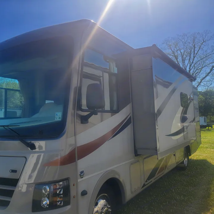 Side view of a light-colored RV rental with its slide-out extended, parked on green grass under a bright sunny sky.. Forest River Coachmen Pursuit 2017