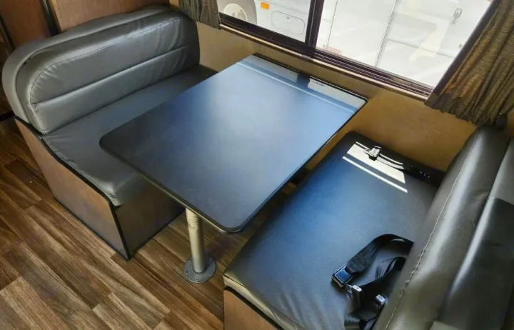 RV rental dinette: dark benches with seatbelts, a black table, and window view for comfortable travel & dining.. Thor Majestic 2019
