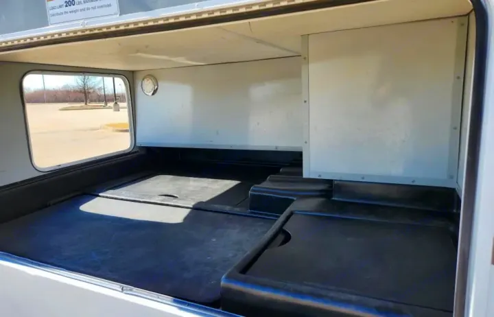 Spacious RV rental exterior storage compartment. Shows a large, empty bay with black floor liners and a side window.. Thor Majestic 2019