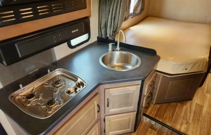 Compact RV rental interior featuring a kitchenette with sink & stove, plus a cozy bed/seating area. Ideal for travel.. Thor Majestic 2019