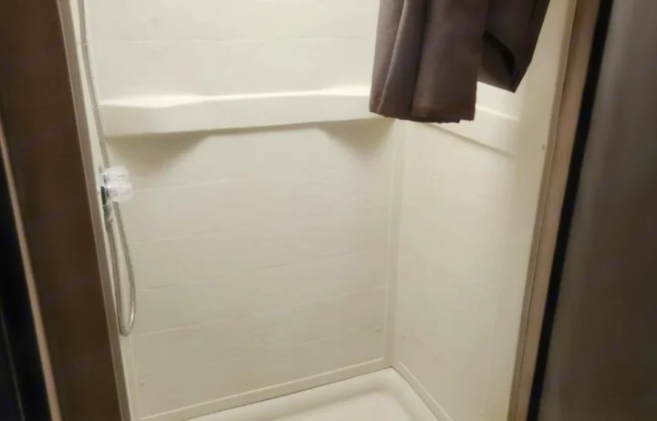 Interior of a compact, clean shower unit found in an RV rental, featuring a handheld showerhead and practical shelf.. Thor Majestic 2019