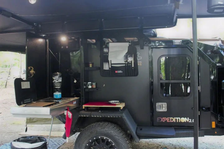 A rugged black Expedition 2.0 off-road trailer with an open side revealing an integrated outdoor kitchen, ideal for rv rental adventures.. Off Grid Trailers Off Grid Trailers Trailer 2021