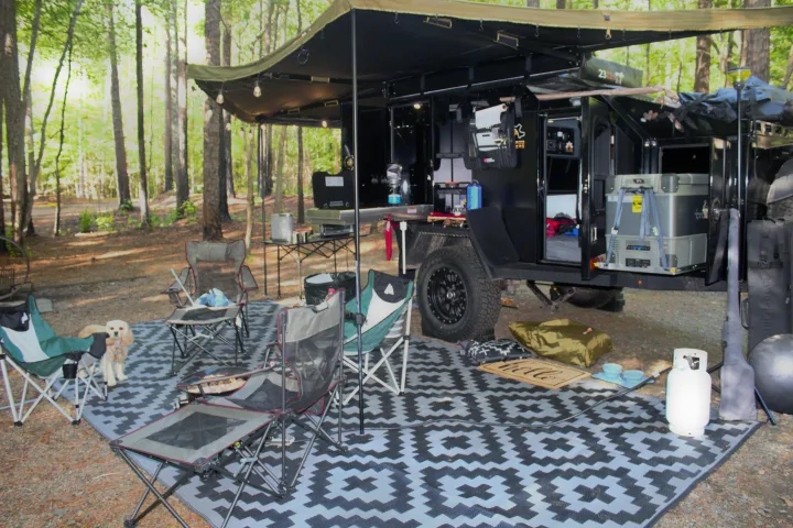 Ultimate outdoor living with this modern overland RV rental setup: kitchen, comfortable chairs, and a happy dog at a serene campsite.. Off Grid Trailers Off Grid Trailers Trailer 2021