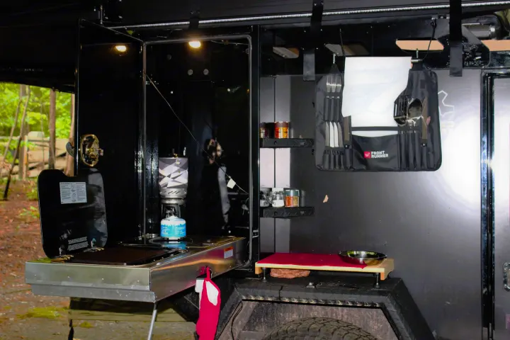 This RV rental features a well-equipped outdoor camp kitchen. Visible are a stove, utensils, spices, and a small prep area, ready for cooking.. Off Grid Trailers Off Grid Trailers Trailer 2021