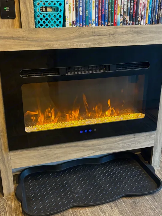RV rental: Cozy electric fireplace glows beneath a shelf of DVDs and a USB charger. A shoe mat is on the floor.. Forest River Cherokee Alpha Wolf 2021