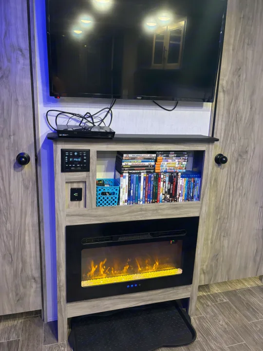 Cozy RV rental interior with a TV, media console, DVD collection, and an electric fireplace for comfortable entertainment.. Forest River Cherokee Alpha Wolf 2021