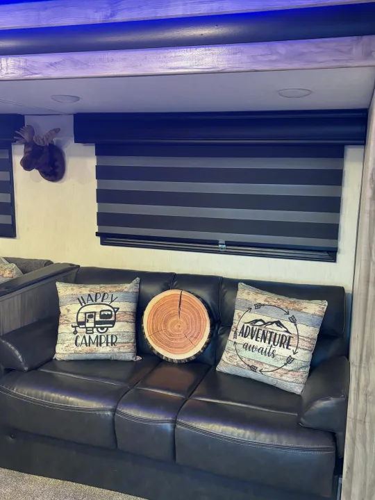Plush RV rental interior: black leather sofa, "Happy Camper" pillows, moose decor, and adjustable window blinds.. Forest River Cherokee Alpha Wolf 2021