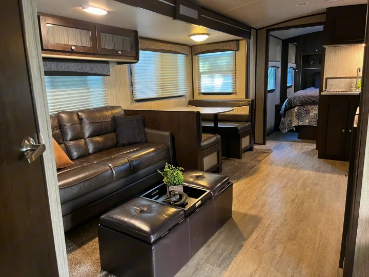Modern RV rental interior featuring a dark sofa living area, dining booth, and cozy bedroom view.. Cruiser RV Shadow Cruiser 2019