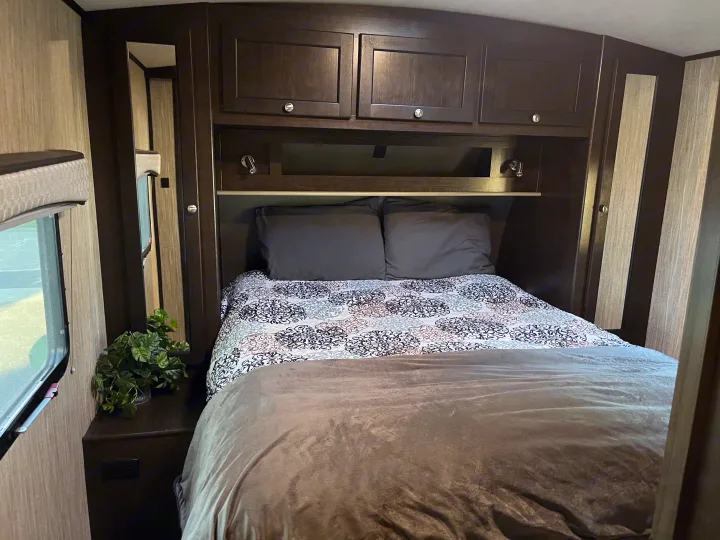 Comfortable RV rental bedroom with a bed featuring patterned bedding, dark wood overhead cabinets, and functional lighting.. Cruiser RV Shadow Cruiser 2019