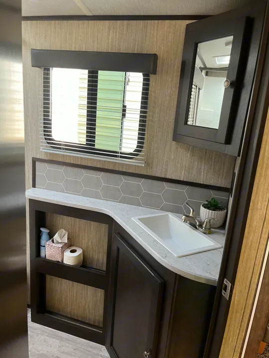 RV rental bathroom with vanity, sink, mirror, window with blinds, hexagon backsplash, and open storage.. Cruiser RV Shadow Cruiser 2019