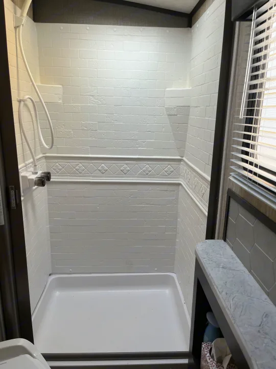 Bright, clean shower stall with white brick-patterned walls in an RV rental. Features a handheld shower and small counter with blinds.. Cruiser RV Shadow Cruiser 2019