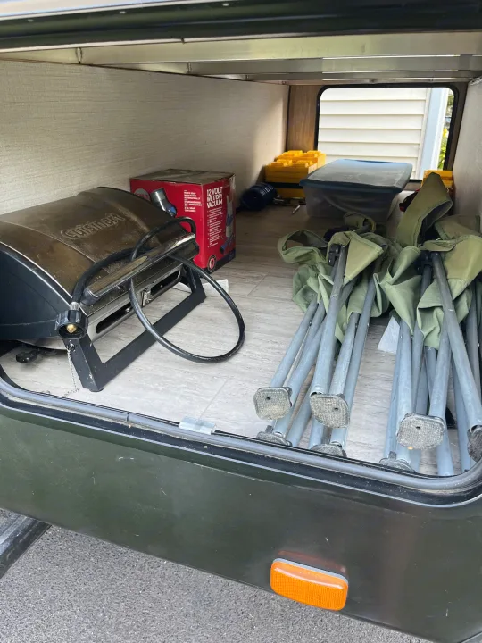 Inside an RV rental's storage compartment, camping gear is organized, including a Cuisinart grill, a vacuum, bin, and chairs.. Cruiser RV Shadow Cruiser 2019