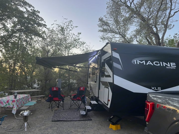 Spacious RV rental campsite with a Grand Design Imagine trailer, picnic area, chairs, and grill. Peaceful outdoor camping.. Grand Design Imagine XLS 2024