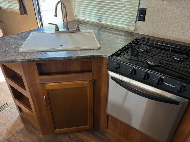 Inside an rv rental: a compact kitchen featuring a sink, faucet, and a black Suburban gas range/oven with a marbled counter.. Keystone Springdale 2017