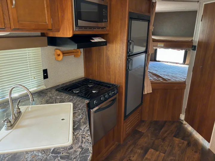 RV rental interior: compact kitchen with sink, stove, microwave, fridge, and adjacent bunk beds.. Keystone Springdale 2017