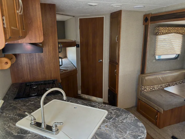 View of an RV rental's interior, featuring a kitchen with stove and sink, bunk beds, and a dining booth with a window.. Keystone Springdale 2017