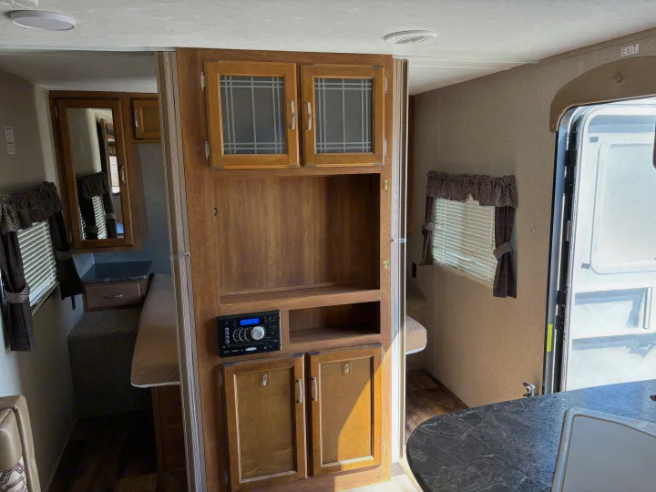 Spacious RV rental interior featuring a central entertainment unit, cozy bedroom, and compact kitchen area.. Keystone Springdale 2017