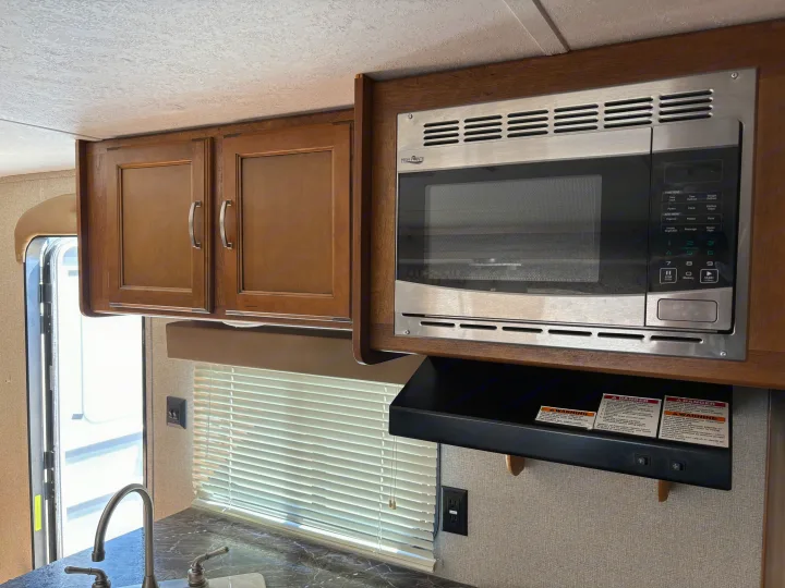 RV rental kitchen interior featuring a microwave, wooden cabinets, sink, and window with blinds.. Keystone Springdale 2017