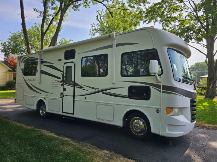 This spacious white motorhome, branded "ACE", is parked on a paved driveway under green trees. Great for an RV rental.. Thor 29.1 2012
