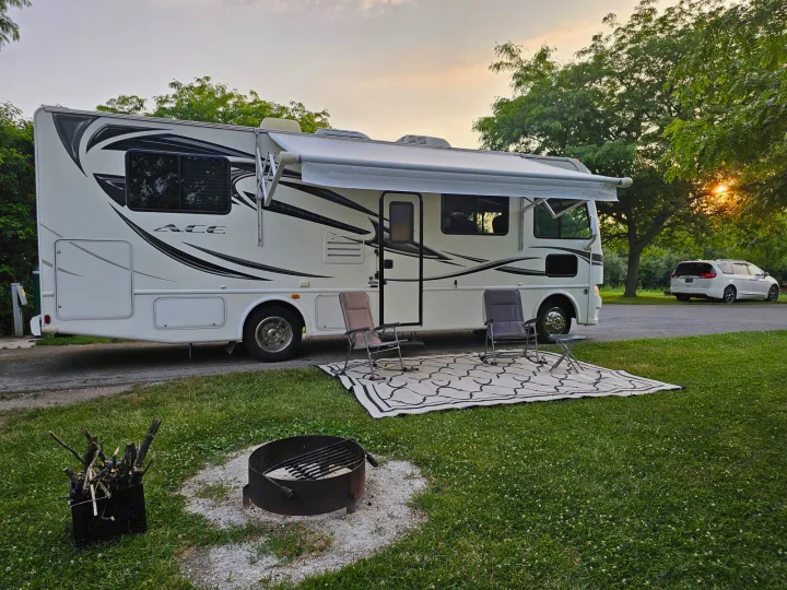 White RV rental motorhome with extended awning, two chairs, and a fire pit at a scenic campsite. Perfect for camping.. Thor 29.1 2012