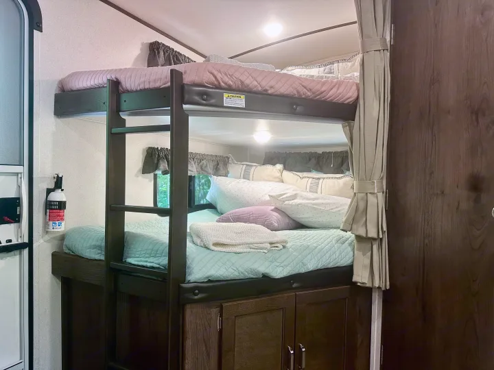 Cozy RV rental bunk beds, fully made with plush pillows, a fire extinguisher mounted nearby.. Keystone RV Passport Grand Touring 2020