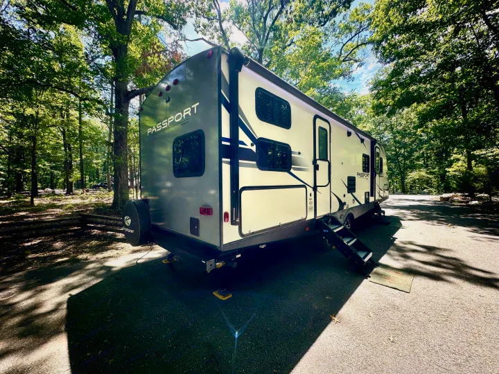 Camping with an RV rental: A Passport travel trailer nestled in a sun-dappled, wooded campsite.. Keystone RV Passport Grand Touring 2020