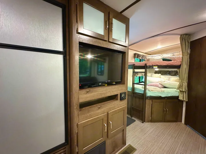 Spacious RV rental interior featuring a TV entertainment unit, refrigerator, and comfortable bunk beds with colorful bedding.. Keystone RV Passport Grand Touring 2020