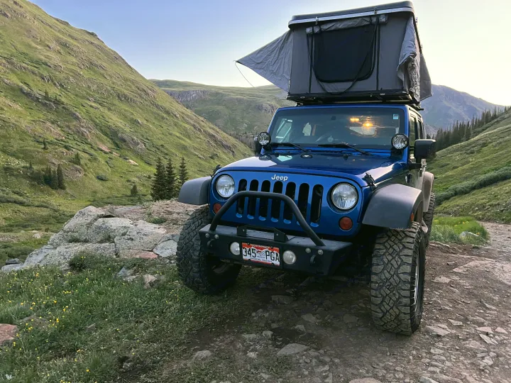 Blue Jeep with rooftop tent on mountain trail. Perfect for off-grid adventure, like an RV rental for rugged exploration.. Jeep Wrangler 2010