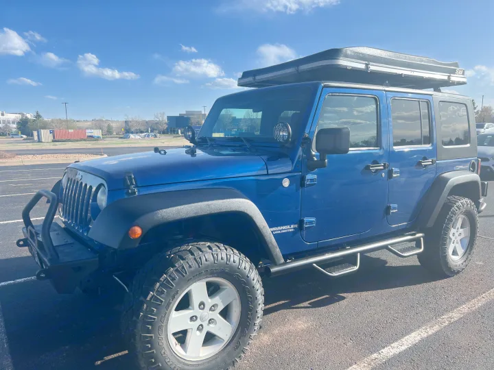 Blue Jeep Wrangler Unlimited with hard-shell rooftop tent, great for outdoor adventure or RV rental camping.. Jeep Wrangler 2010