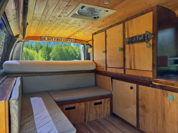 Cozy custom RV rental interior with wooden accents, built-in storage, and a view of nature. Perfect for travel adventures!. Ford Ford E350 1996