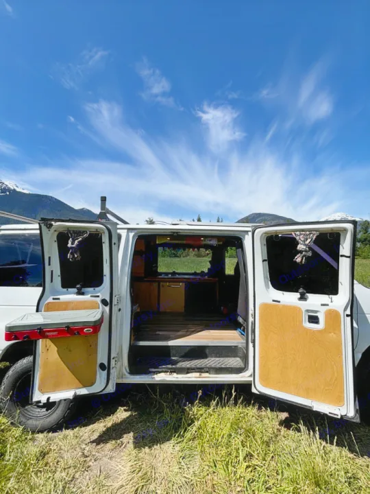 Open doors of a customized campervan with a cooking station, parked in a scenic mountain setting. Perfect for your next RV rental adventure.. Ford Ford E350 1996