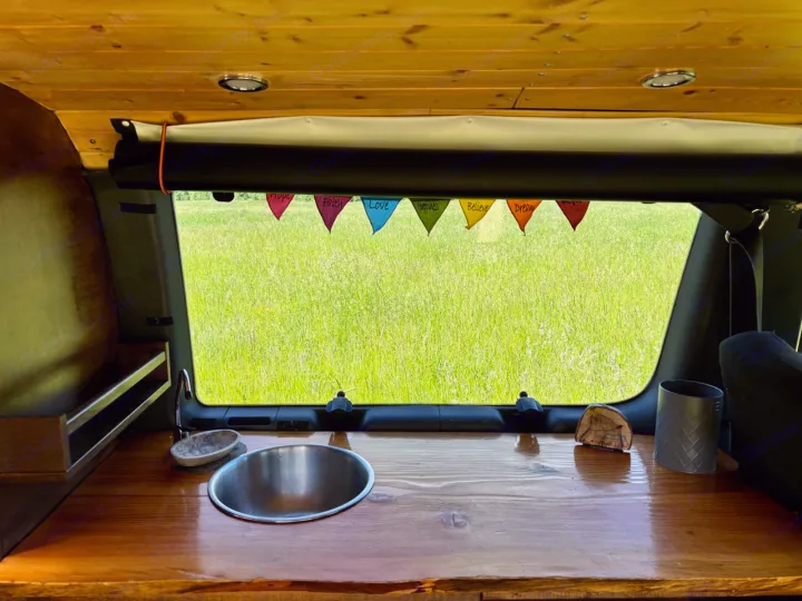 Discover the interior of an RV rental: a warm wood kitchen with sink, comfy setup, and window with pennant flags facing nature.. Ford Ford E350 1996